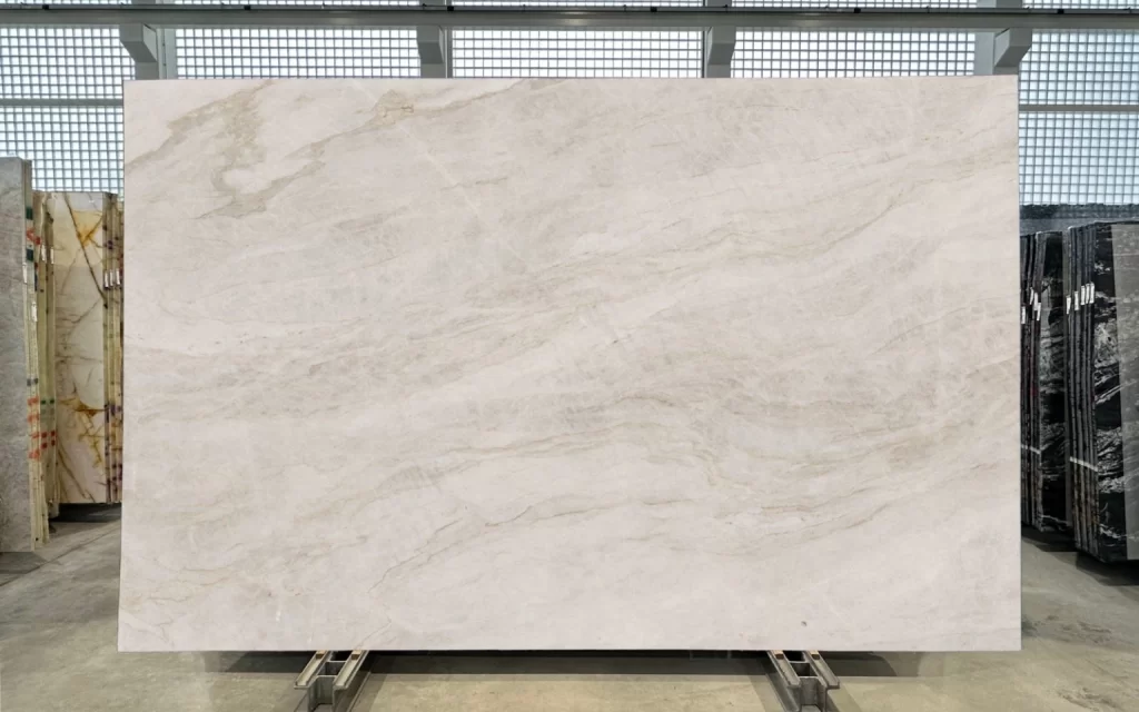 A large rectangular slab of white marble with subtle grey and beige veining, reminiscent of the elegance found in the Taj Mahal, is displayed upright in Block 1 of the showroom. The background features other slabs with diverse colors and patterns.