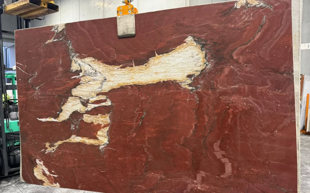 A large, polished slab of red marble with white and yellow veins, resembling the unique patterns of Jasp, clamped vertically in a workshop setting.