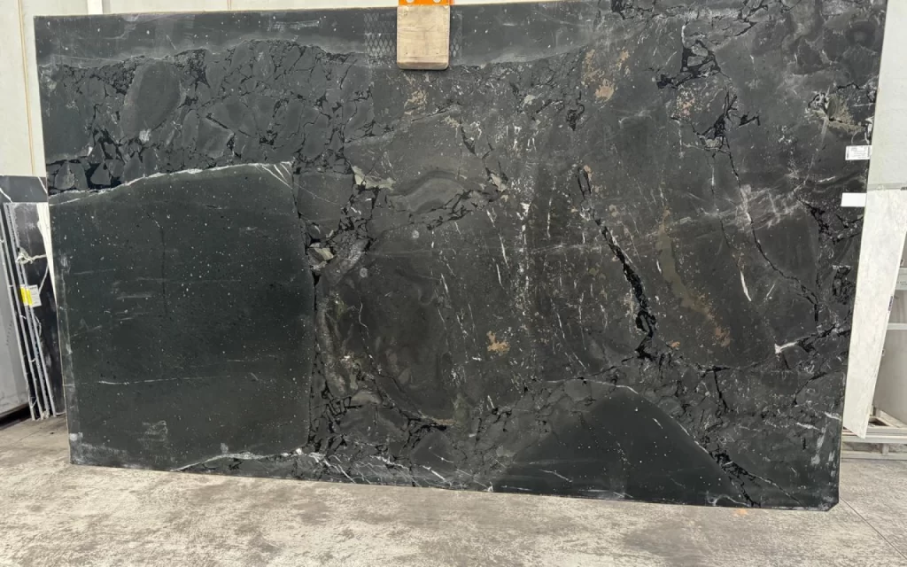 A large, polished Negreso Black marble slab with striking white and gray veining is displayed upright in an indoor space, resting elegantly on a concrete floor.