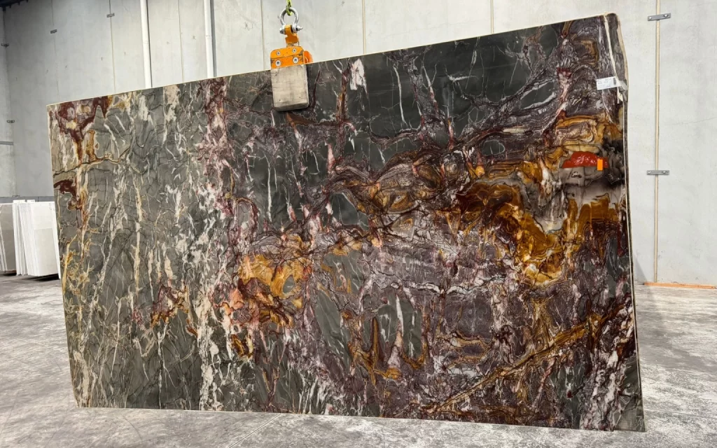 A large slab of polished natural stone with various shades of grey, red, yellow, and white patterns stands upright in an industrial setting, reminiscent of a scene from a Marvel film.