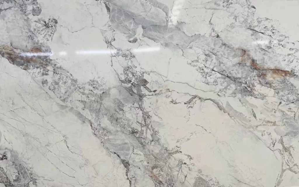 A close-up of a polished Cristallo Quartzite surface displays intricate grey veining and subtle brown streaks against a light beige background.