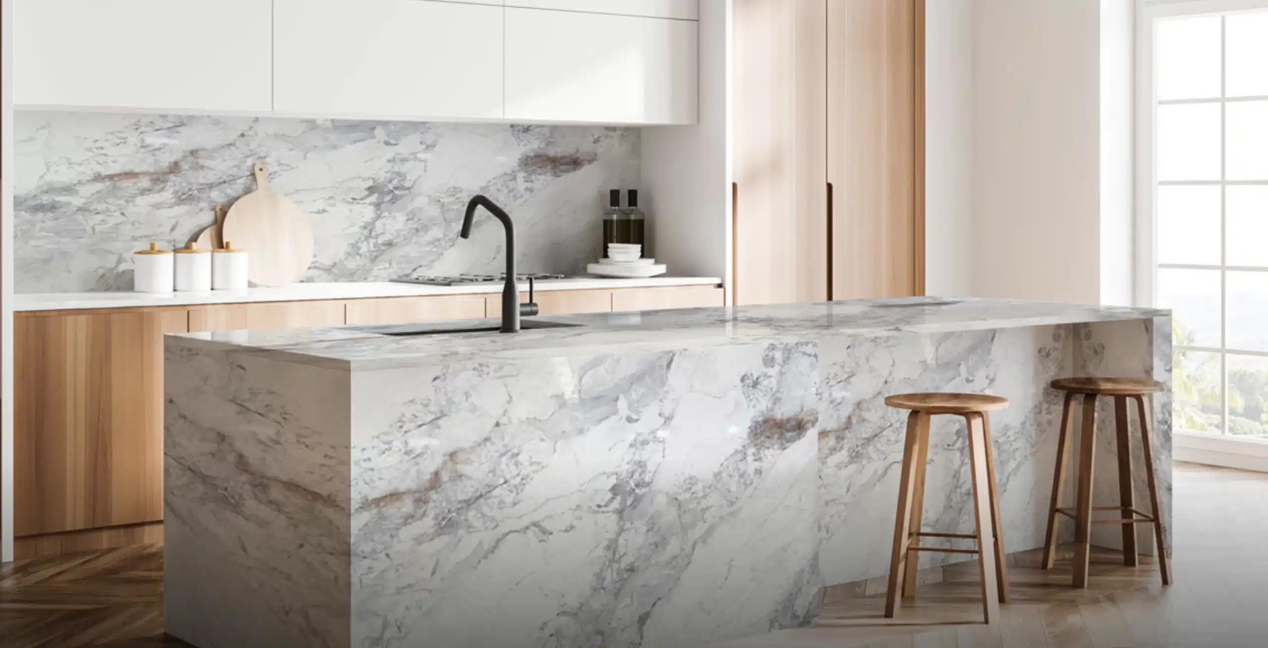 Modern kitchen with white marble countertops and backsplash. Black faucet on the island with a wooden bar stool and minimalist design elements.